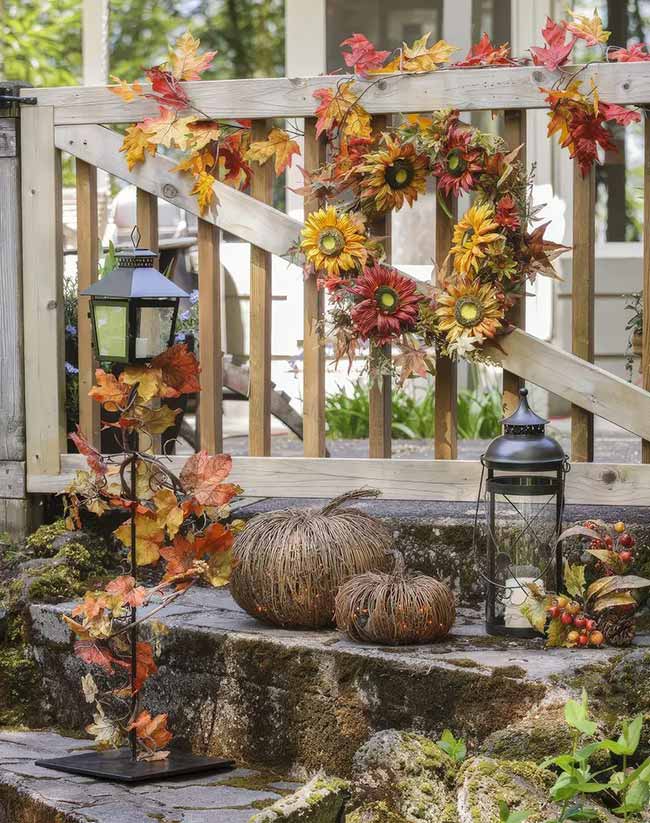 This is a whole setup! The dark lanterns are placed on the stone steps next to the railing, which is covered in a fall leaf garland and a sunflower wreath. The two large, round twig pumpkins make this a welcoming and textural Fall Lantern Decor idea for an outdoor space.
