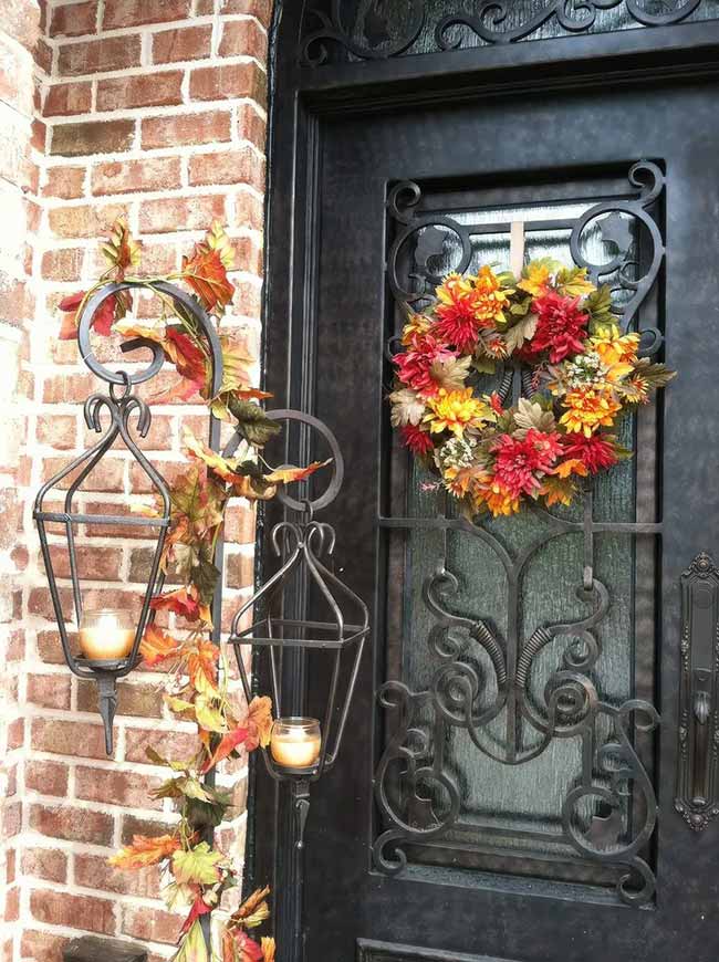 These two black wall sconce lanterns hang right beside a fancy black door decorated with a wreath of bright red and yellow flowers. Wrapping the metal hangers with an orange and green leaf garland is an easy way to make these outdoor lights part of your fall decor look.