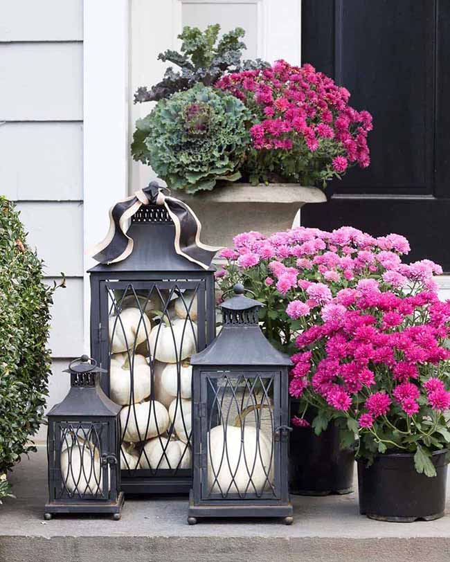 This is a fun idea for the porch—a set of three black metal lanterns with a wire cage design, all filled with smooth white pumpkins. Putting them next to the big, bright pink mums creates a stylish color pop that really catches the eye.