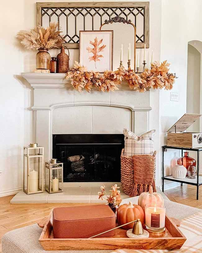 These two modern gold and glass lanterns sit on the hearth for a glamorous look. The mantel above has a beautiful fall garland draped over it, making the whole fireplace area feel bright and cozy.
