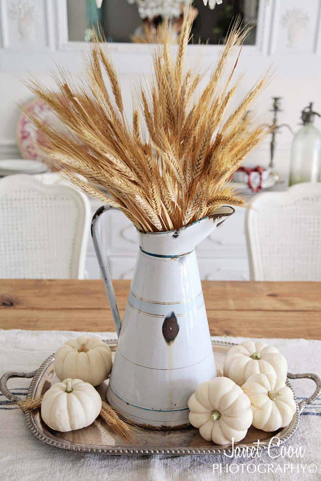 There is a special charm in simple farmhouse decor. A handful of mini white pumpkins scattered around an old metal pitcher filled with wheat creates a centerpiece that is both rustic and incredibly beautiful.