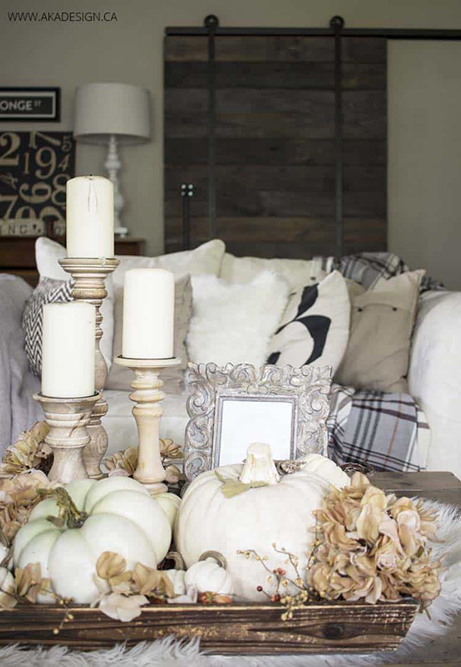 A wooden tray is the perfect base for creating a cozy fall scene on your coffee table. The soft look of a white pumpkin mixed with dried flowers and warm candles makes the whole living room feel more inviting.