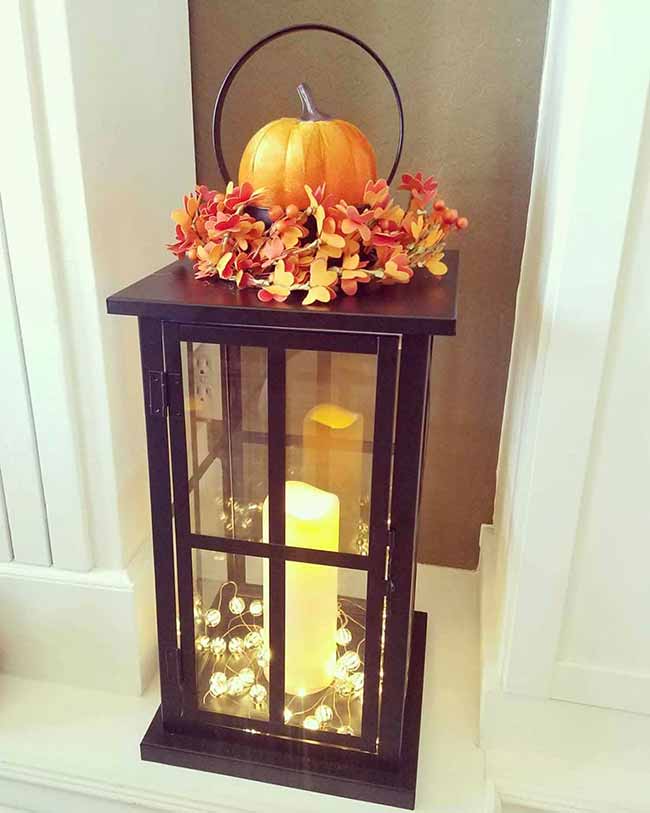 This tall, dark lantern has a candle inside and is wrapped with small white fairy lights for a sweet, magical look. Topping it with a little orange pumpkin and red-orange flowers makes it a simple but stunning Fall Lantern Decor piece for a corner.