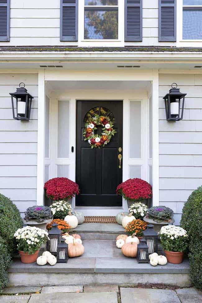 The outside wall lanterns next to this dark door are a perfect match for the black lanterns and pumpkins below them. This whole front step area is covered in mums and pumpkins for a layered, inviting fall porch display.