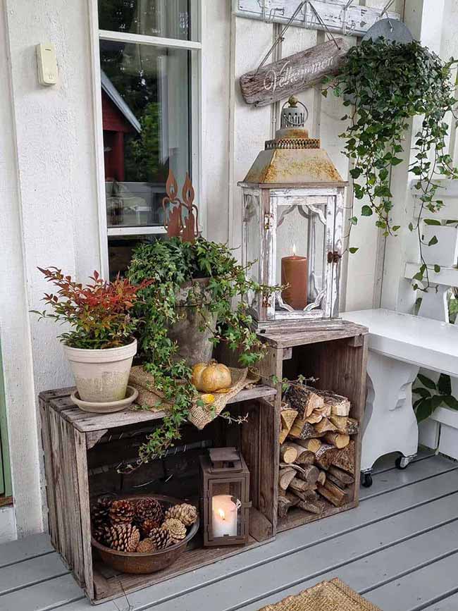 This is a great little porch vignette made from stacked wooden crates holding wood logs, pinecones, and small lights. The distressed white lantern with the chunky brown candle sits right on top, creating a perfect rustic fall scene.