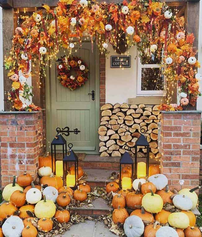 This is a huge, stunning entryway! The doorway is wrapped in an arch of fall leaves and little white pumpkins with fairy lights. Two tall black lanterns sit on the brick porch among a giant pile of harvest pumpkins.