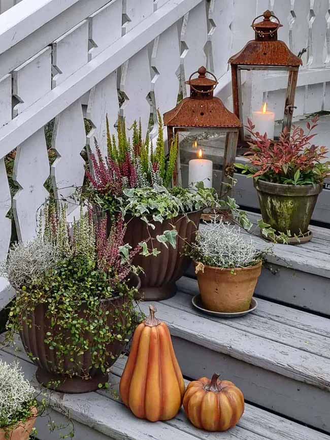 This gorgeous outdoor staircase is decorated with planters full of deep red and green plants, along with weathered copper lanterns. The white candles inside give off a soft glow, making the chunky orange pumpkins on the steps look inviting.