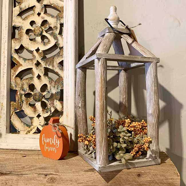 This light, rustic lantern is made from weathered wood sticks and is filled with pale green faux succulents and orange berry clusters. It looks lovely next to that carved white frame and the orange 