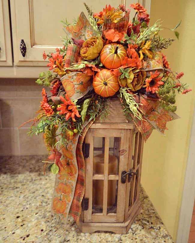 Someone got creative by covering this simple wood lantern with a huge, gorgeous floral arrangement. It's full of sunflowers, deep red flowers, two small pumpkins, and a wide pumpkin-patterned ribbon, making this tall lantern stand out as a centerpiece.
