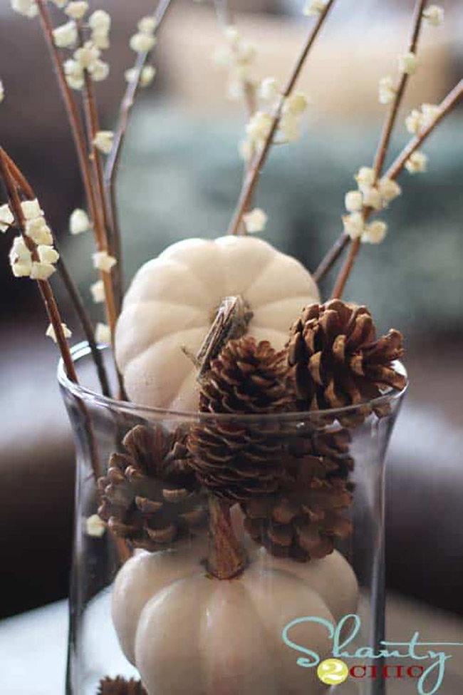 They put small white pumpkins and brown pinecones inside a clear glass with some delicate white flower sticks coming out. It’s a simple, cozy centerpiece that really highlights the little white pumpkin.