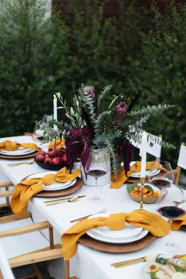 The dark flowers really stand out as a centerpiece against the white tablecloth. Those mustard-yellow napkins add the perfect pop of autumn color to this elegant table setup.