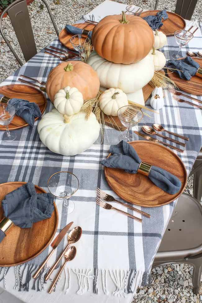 The combination of a plaid tablecloth, wooden chargers, and copper flatware makes for a perfectly cozy and stylish outdoor fall table. Stacking pumpkins in the center is a simple trick that makes a big impact.
