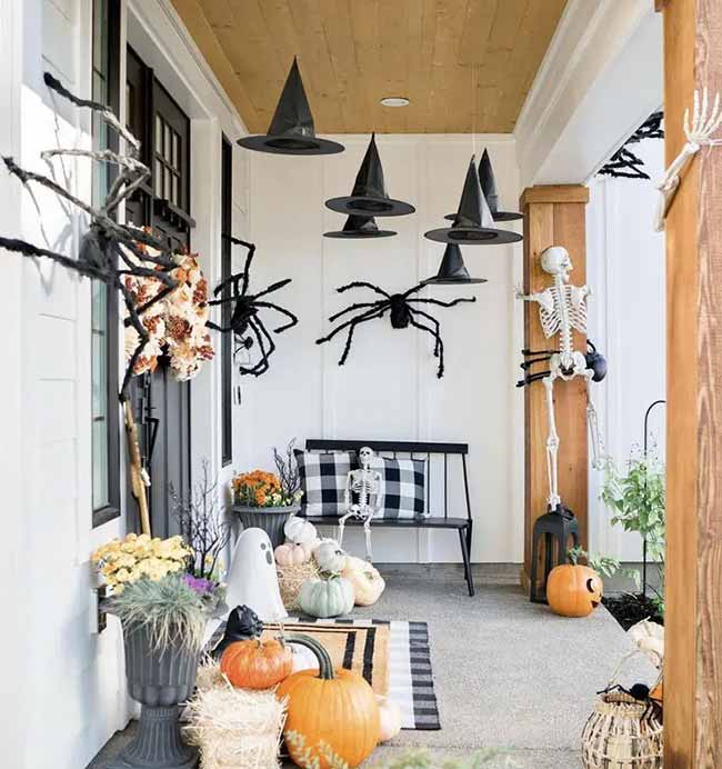This porch is ready for Halloween with skeletons, big spiders, and pumpkins. Hanging the witch hats from the ceiling is the perfect finishing touch.