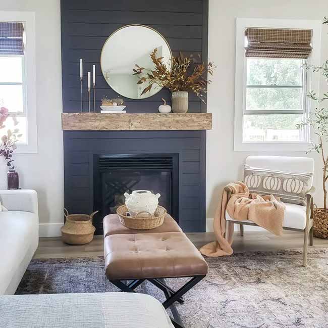 The dark wall behind the fireplace looks so good next to the white walls. I like how they used a simple bunch of fall leaves and a little white pumpkin on the mantel. The leather ottoman makes the whole room feel warm.