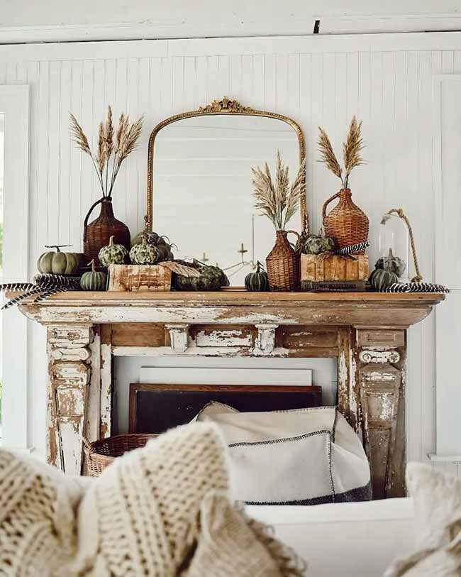 What a cool, weathered fireplace! The chipped white paint and the rustic wooden mantel are full of charm. The arrangements of pampas grass and woven pumpkins on the mantel feel very natural and simple for the season.