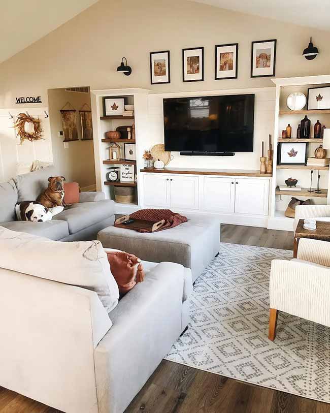 The built-in shelves next to the TV are decorated beautifully with simple fall things. Small leaf-print pictures and dark bottles are mixed with tiny orange and white pumpkins. The dogs on the couch are definitely making the room extra cozy!