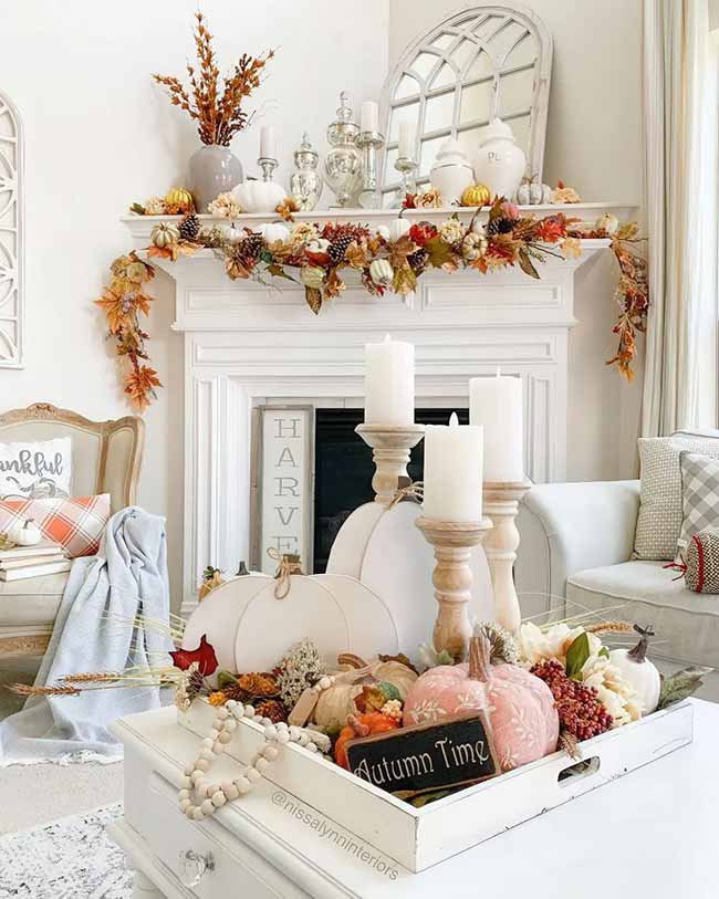 This white mantel is dripping with a gorgeous, colorful leaf garland. The centerpiece tray on the coffee table features soft pink and white pumpkins and big white candles. This is a very elegant, feminine way to decorate for fall.