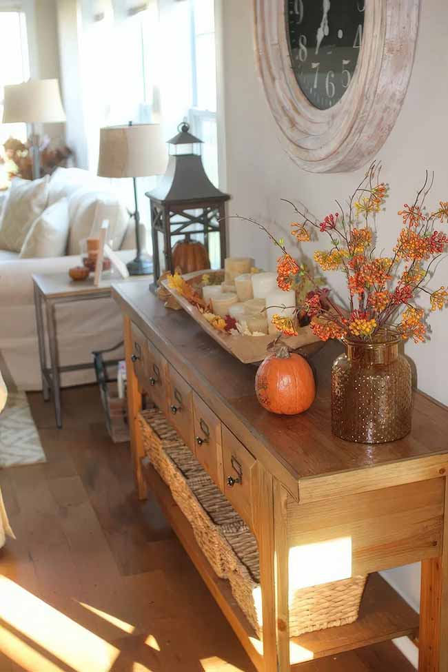 The bright sunshine on this wooden console table makes the orange berry branches glow. I love the old clock and the big lantern sitting next to the simple pumpkin and candle tray. The whole setup feels warm and very welcoming.
