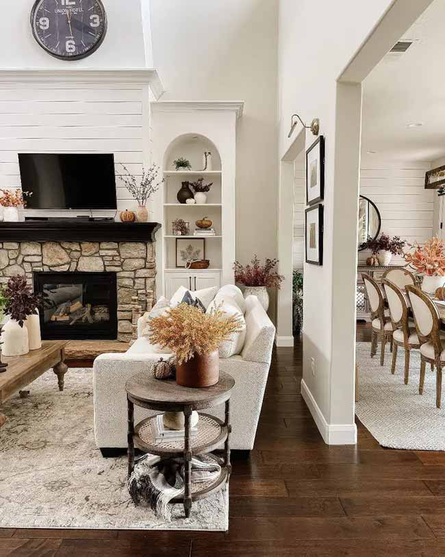 This living room has high ceilings, a gorgeous stone fireplace, and white shiplap walls. The small wooden side table with dried grasses is the perfect cozy touch next to the light-colored sofa. It’s a clean look that still feels ready for fall.