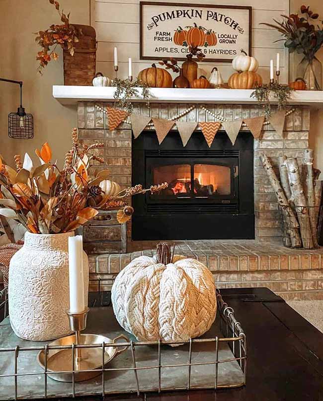 The brick fireplace has a big 'Pumpkin Patch' sign and a cute fabric banner hanging below the mantel. The large, braided rope pumpkin on the tray is a fun centerpiece. Everything is perfectly set up for a warm, fall night.