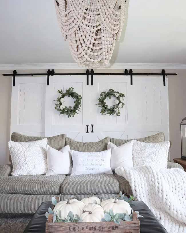 The two white barn doors on the wall are a cool feature and the simple green wreaths look great on them. The white pillows and chunky throw make the striped gray couch look super comfy. The wooden crate full of white pumpkins is a perfect table display.