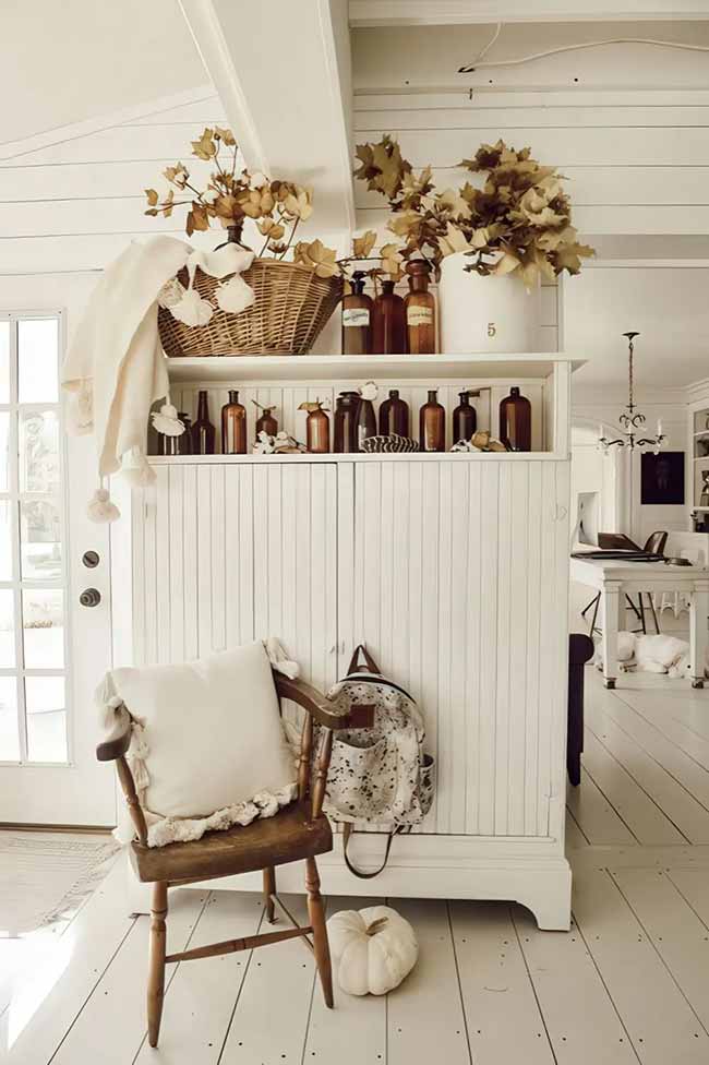 The small antique cabinet is decorated with a bunch of cool brown glass bottles and dried leaves. The old wooden chair with the white pillow looks like a sweet little spot to sit down. This room is bright and simple but still has a lot of farmhouse charm.