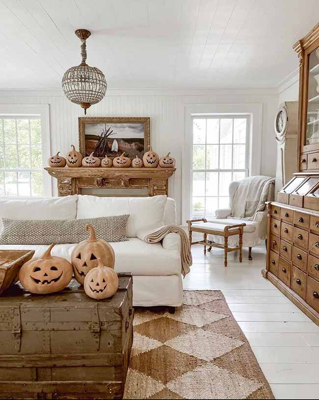I like how this rustic room mixes the Halloween jack-o'-lanterns with a very soft, farmhouse style. The row of smiling pumpkins on the old wooden mantel is so fun. The big white sofa and antique wood furniture keep the room light and airy.