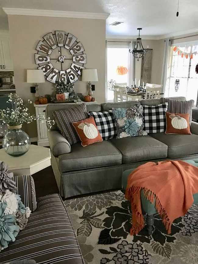The big, rustic clock on the wall is a great centerpiece in this room. The mix of buffalo check and stripe pillows gives the couch a classic farmhouse feel. The bright orange throw brings the perfect amount of autumn color to the sofa.