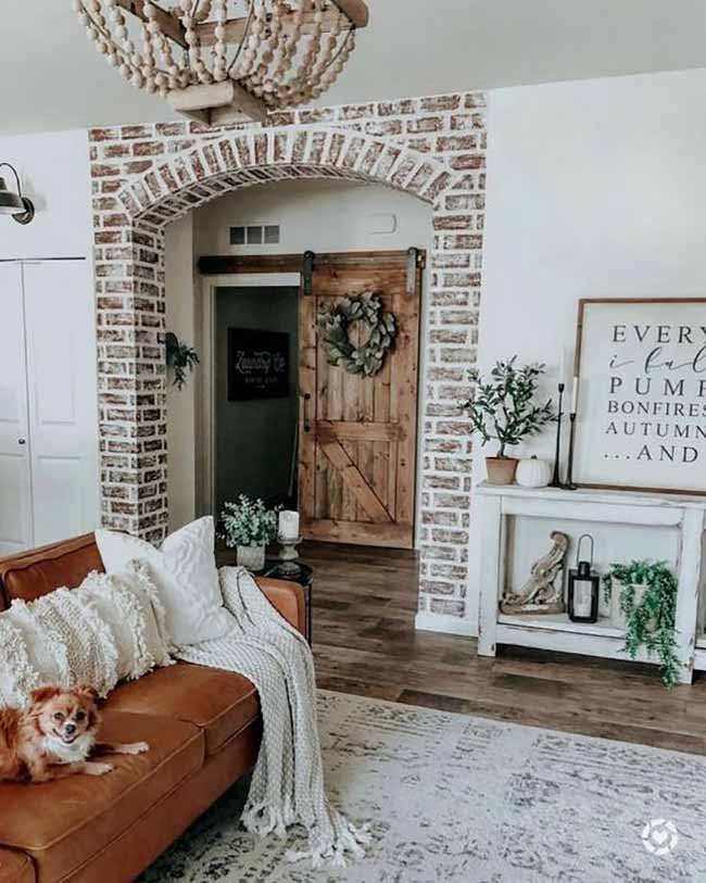 The exposed brick archway and rustic wooden barn door add so much character. The big brown leather couch with the chunky white blanket is what fall comfort is all about. The sign on the console table has a sweet autumn message.