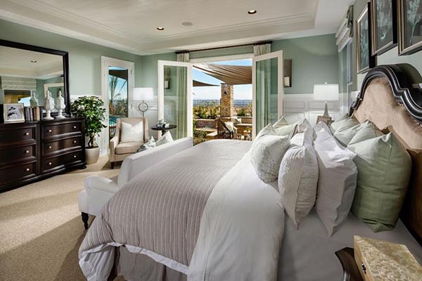 A lovely white chase lounge is perfectly positioned at the foot of the bed, creating a neat sitting area that leads the eye toward the French doors and the sunny patio view. The light green walls and crisp white trim give this master suite a fresh and airy feel.