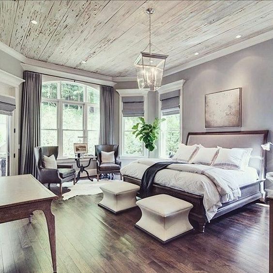 The expansive master suite features a small, intimate sitting area tucked in the large bay window, using two stylish leather chairs. This cozy nook is separated from the main sleep space by the bed, offering a private place for reading under the beautiful rustic wood ceiling.