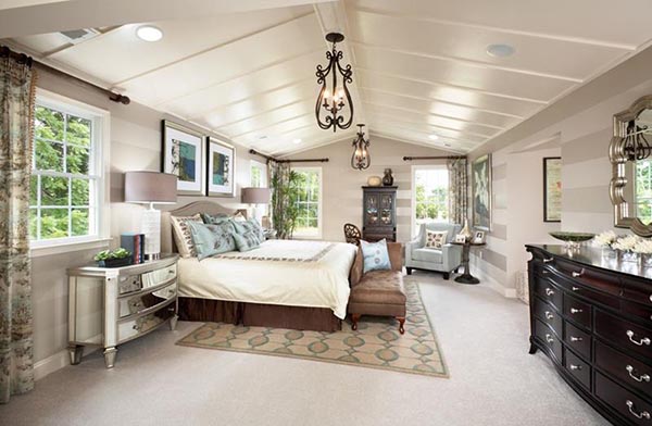 This bright and spacious master bedroom is thoughtfully laid out with a plush, comfortable sitting chair and side table in the corner. This setup creates a small, dedicated retreat area, balanced by the beautiful vaulted ceiling and natural light.