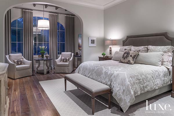 The master suite achieves a true separation between spaces by placing the sitting area within a dramatic arched alcove. Two elegant slipcovered armchairs and a small table make this nook feel like a quiet, intimate room all its own.