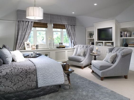 The calm, soothing gray tones make this master bedroom feel like a true retreat. Across from the bed, the dedicated sitting area features two elegant light gray barrel chairs facing a media console, which makes the whole space feel like a relaxing, cozy lounge.