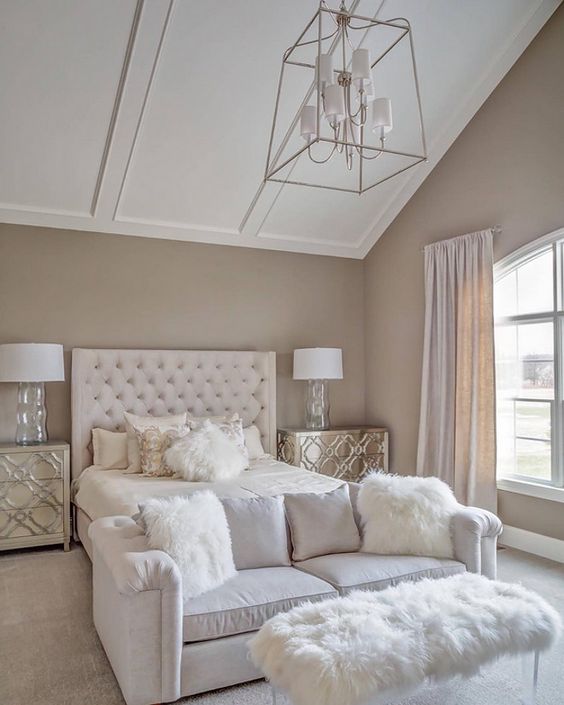 Opulence defines this beautiful master suite. A plush, stylish white loveseat is perfectly placed as a luxurious sitting area at the foot of the bed, with faux-fur pillows adding maximum cozy glamour under the high, vaulted ceiling.