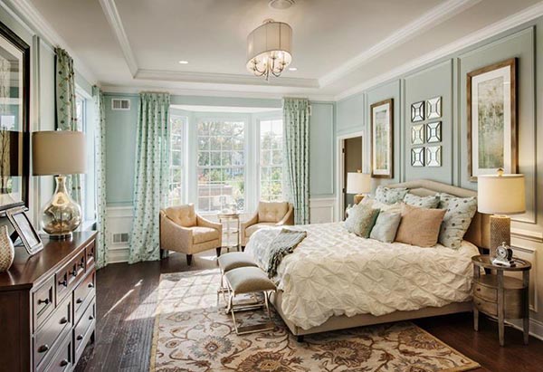 What a wonderfully charming and bright master suite! Two cute yellowish armchairs and a small side table are perfectly nested in the sunny bay window, creating a welcoming sitting area. The light blue walls and patterned curtains add a beautiful, soft coastal feel.