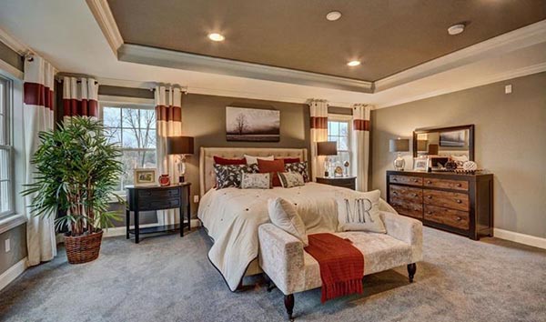 The contrasting dark ceiling and warm red accents make this master bedroom feel incredibly cozy. A small, tufted sitting bench at the foot of the bed, draped with a red throw, offers a lovely place to pause.
