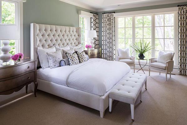 This room uses clean whites and soft greens to create a serene, luxurious atmosphere. The dedicated sitting area by the window features two crisp white wingback chairs and a small X-base table, perfect for quiet conversation while enjoying the bright view.