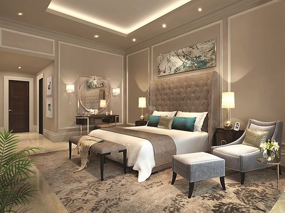 A single, stylish gray velvet armchair and matching ottoman are positioned for easy use, creating a small, luxurious reading spot. The dramatic oversized tufted headboard completes this glamorous look.
