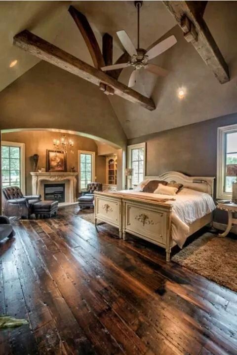 Rustic charm meets luxury in this stunning master retreat! The sitting area is defined by a cozy stone fireplace and two large leather club chairs tucked into the arched nook. The dramatic exposed wood beams on the vaulted ceiling truly complete the cabin aesthetic.