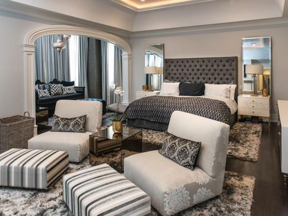 This master suite expertly uses texture and pattern to define its zones. A casual yet chic sitting area is created by two low white club chairs and two bold striped ottomans, clearly separating the lounge space from the sleeping area under the beautiful arched entryway.