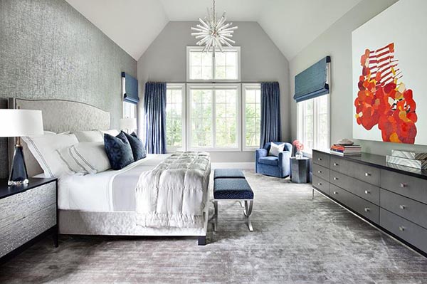 Vibrant blue accents bring a stylish energy to this modern gray master bedroom. The focused sitting area is established by a deep blue accent chair and a geometric side table near the window.
