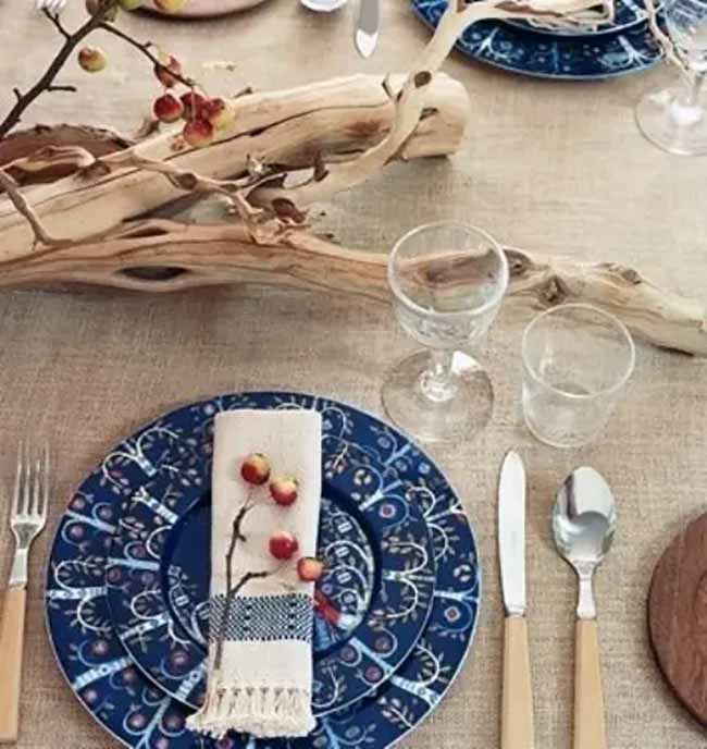 Natural Table Setting. The dinner plates have a beautiful dark blue pattern that looks very unique. The piece of driftwood and the little crabapples tucked into the napkin make the table setting feel very natural and earthy.