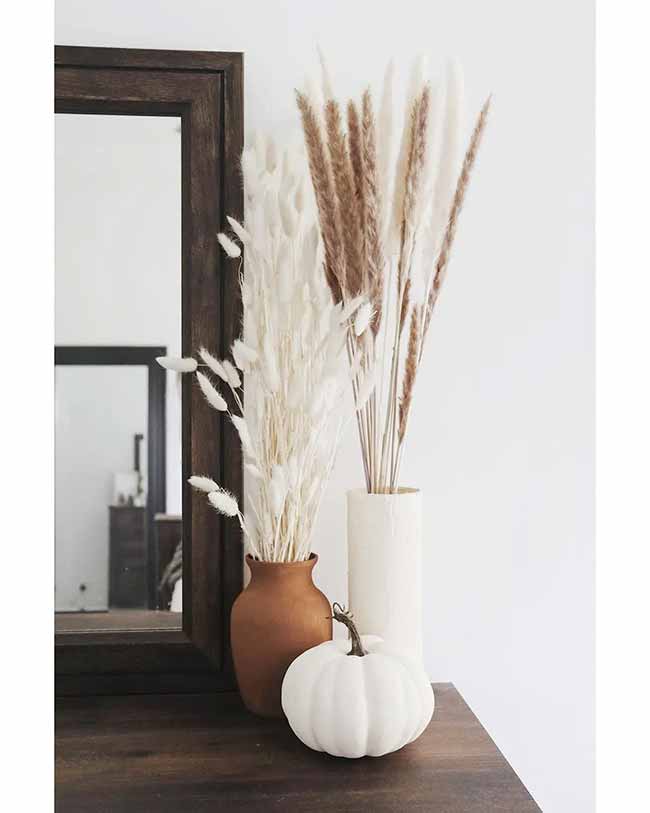 Dried Grass Decor. This arrangement uses different kinds of dried grass and plants in simple vases. The terracotta vase and the white pumpkin sitting next to the dark mirror look very warm and seasonal.