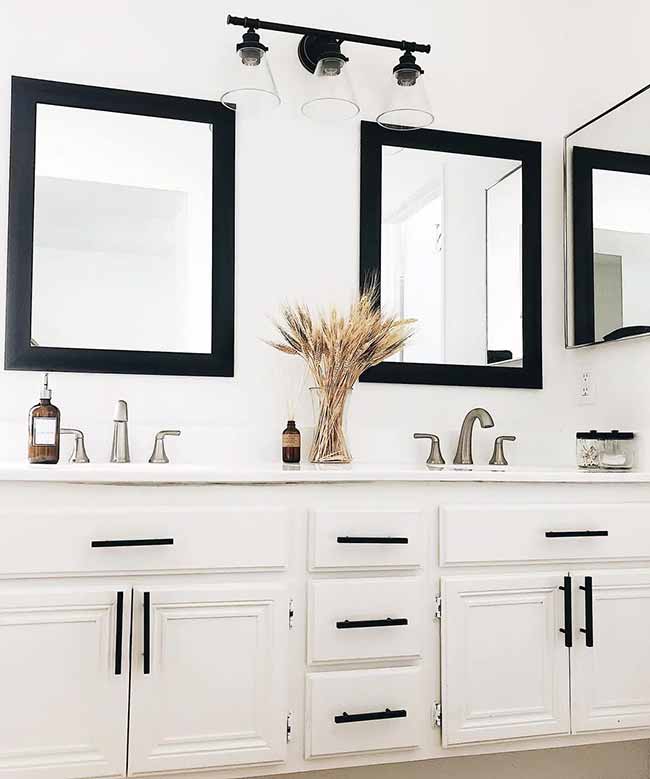 White Bathroom Accents. The simple bunch of dried wheat in the middle brings a nice autumn texture to the bright, clean bathroom. The black frames on the mirrors and cabinets give a great contrast to all the white.