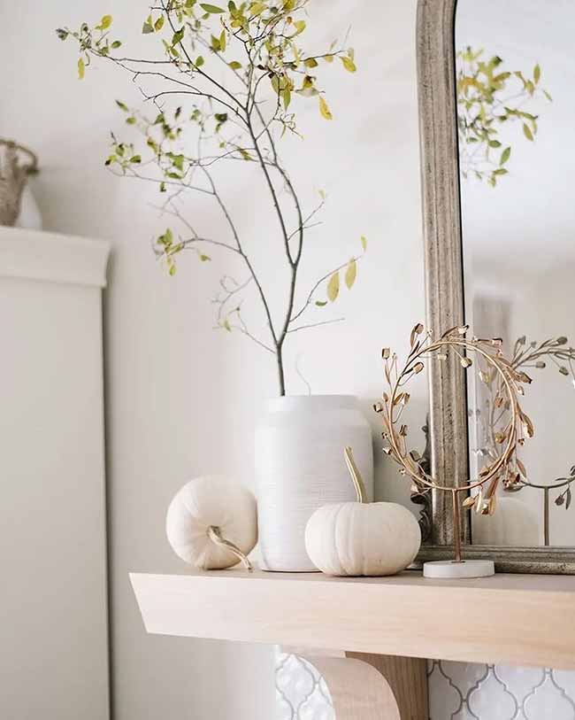 White Mantel Styling. The pairing of the white pumpkins with the simple gold wreath is very elegant. The bare branch in the tall white vase adds a nice, natural height to the display.