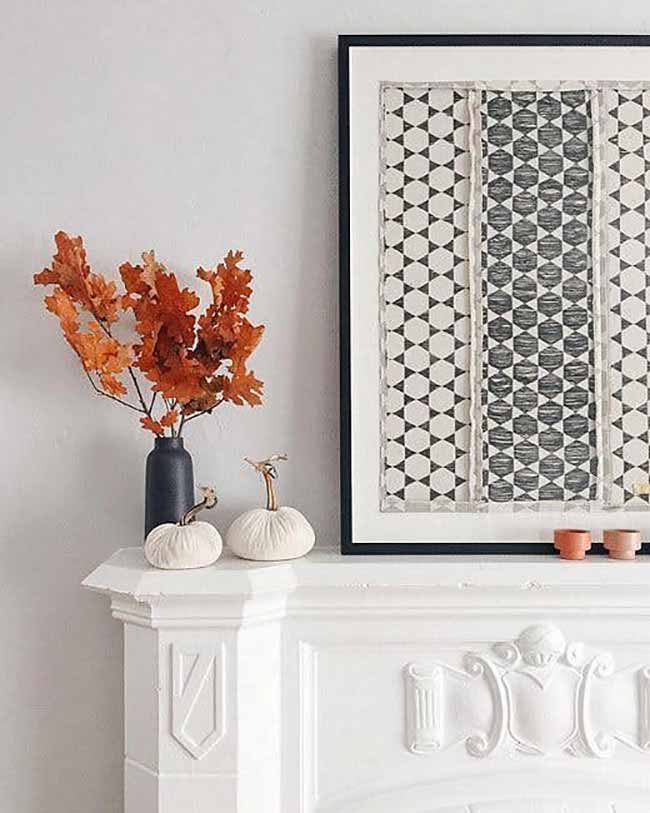 Autumn Mantelpiece. The vibrant orange oak leaves in the dark blue vase give a strong pop of color to the white mantel. The two tiny white pumpkins look so cute next to the large, patterned artwork.