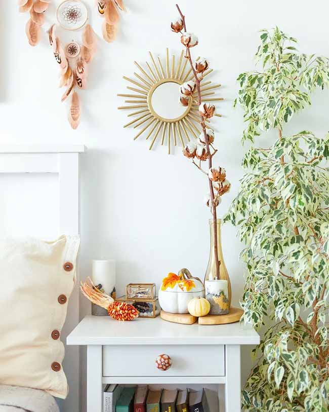 Autumn Bedside Decor. A gold sunburst mirror and fluffy cotton branches decorate this bright nightstand. Small white pumpkins and colorful corn add a nice seasonal touch.