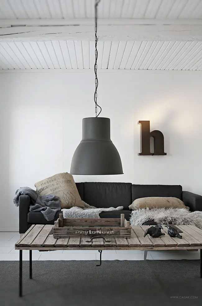 Industrial Lounge Scene. A massive, dark gray pendant light hangs over the sofa, giving the room an industrial edge. The rough wood coffee table and fur throws soften the space.