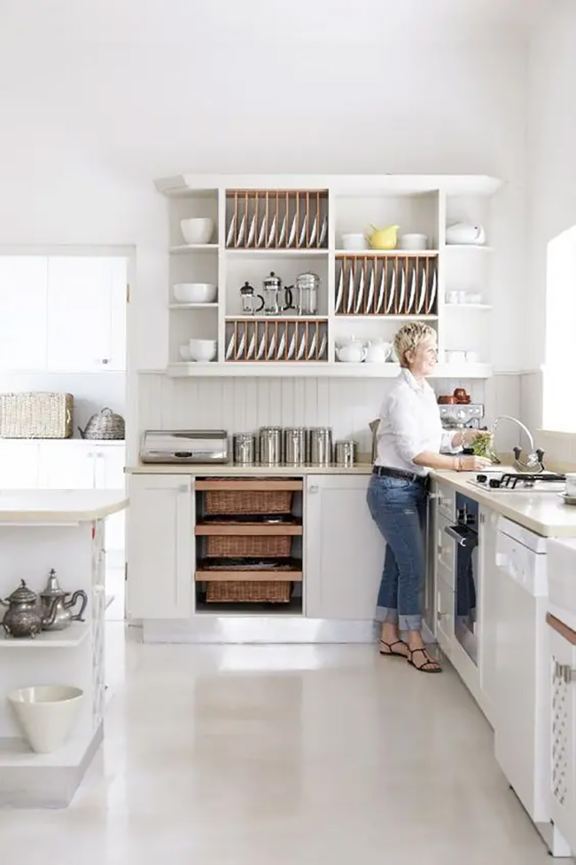 This white kitchen uses open racks to hold plates upright and organized. It looks very neat and makes it easy to grab a dish for dinner. The wicker drawers under the counter are a smart no door kitchen cabinet idea for storing big pots and linens.